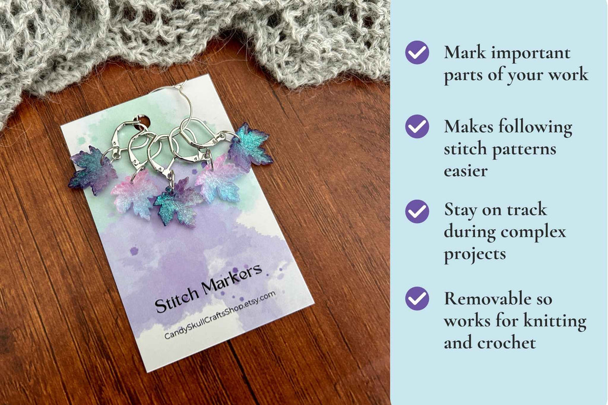 A set of winter frost themed maple leaf stitch markers for knitting and crochet, featuring blue, purple, and pink shimmer colours, presented on a branded card over a wooden surface with a knitted scarf. A light blue text panel on the right lists product benefits. Mark important parts of your work. Makes following stitch patterns easier, stay on track during complex projects. Removable so works for knitting and crochet.