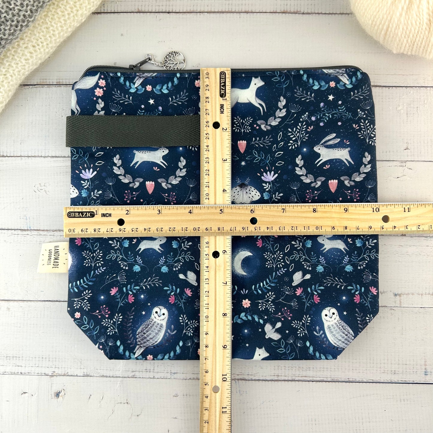 A dark blue knitting or crochet project bag with grey handle & zip. The fabric features nocturnal woodland animals - a hare, fox, moth, and owl. There is a ruler laying across the bag showing it measures approximately 10 inches by 9.5 inches