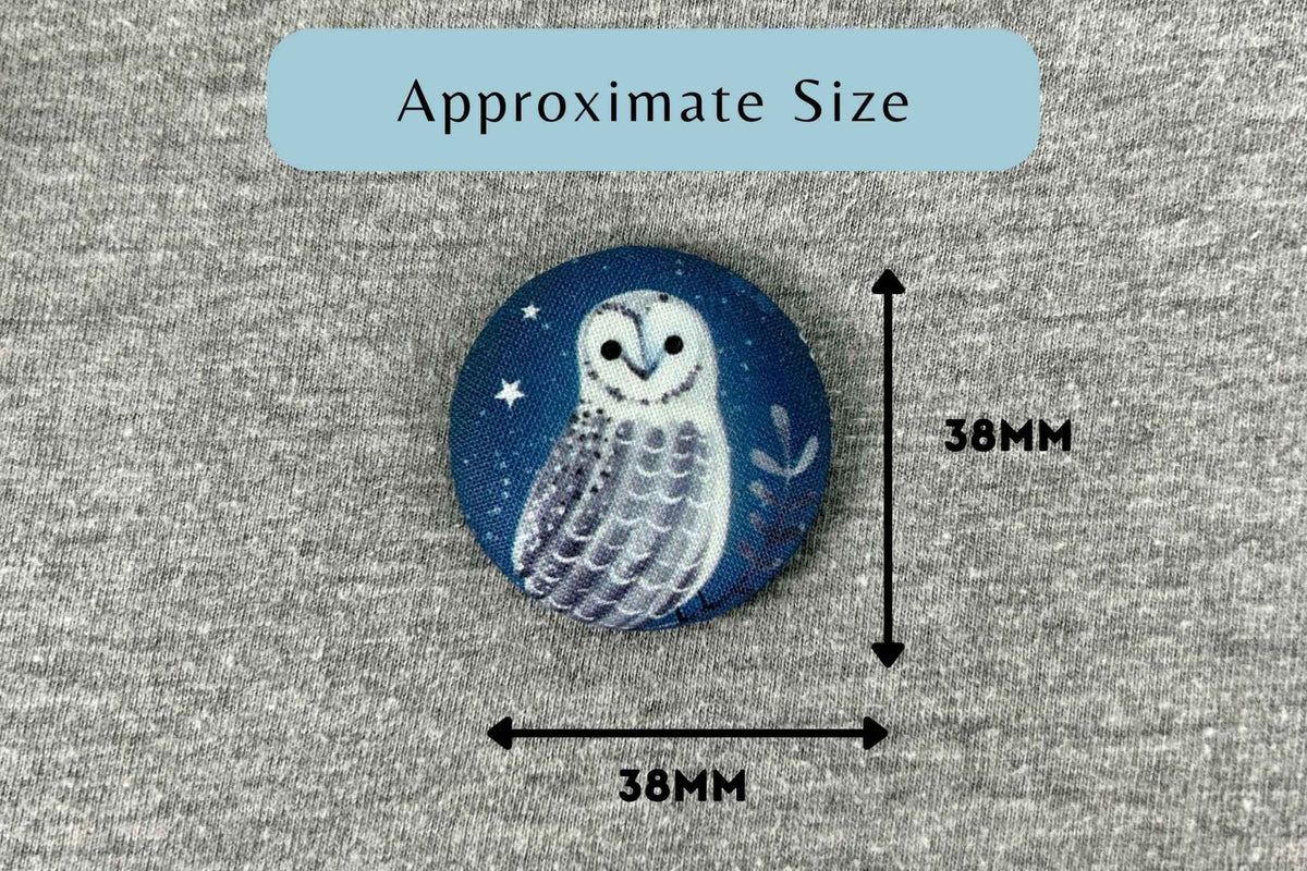 A round fabric magnetic needle minder featuring a painted white owl on a dark blue night-sky background, shown on a gray fabric surface with measurement arrows and text indicating approximate size 38mm by 38mm.