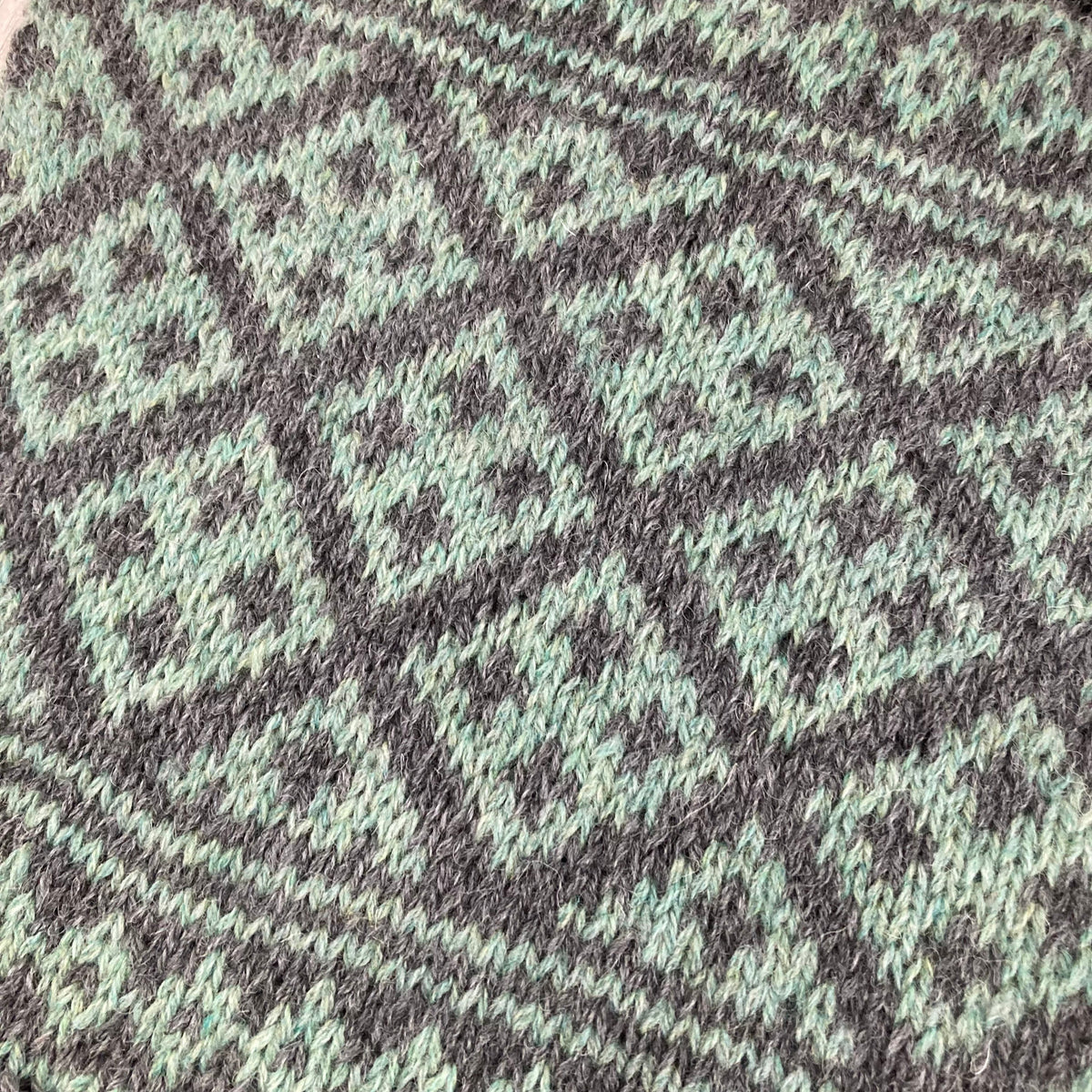 A close up of the geometric Selbu knitting pattern in green and dark grey stranded colourwork