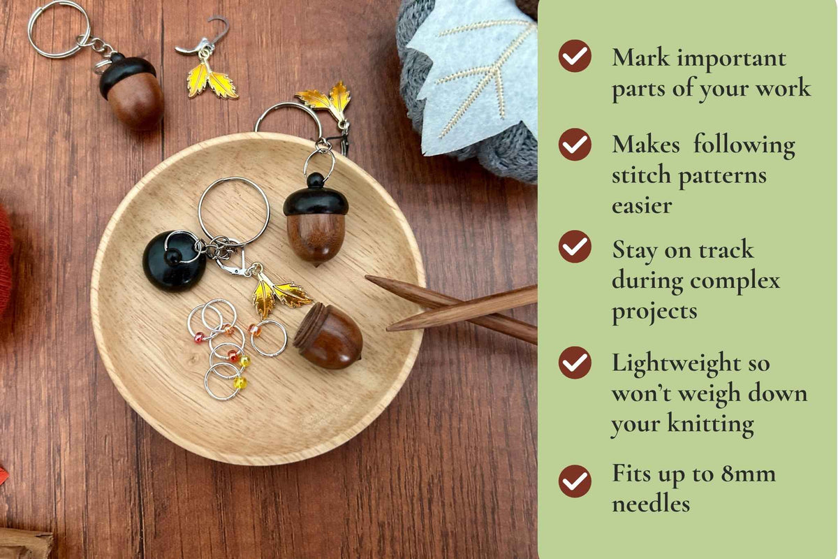 A dark coloured wooden acorn knitting stitch marker holder, opened to up reveal 6 beaded ring knitting stitch markers with red, orange, and yellow beads. There is a removable progress keeper n 2 yellow leaves. All displayed on a light wooden dish. The info graphic reads "mark important parts of your work, makes following stitch patterns easier, stay on track during complex projects, lightweight so won't weigh down your knitting, fits up to 8mm needles. 