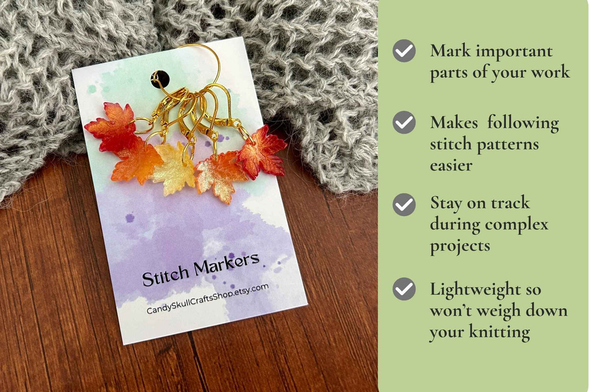A set of gold metal knitting or crochet stitch markers decorated with colourful autumn leaves (orange, red, yellow) on a business card. The card is placed on a wooden surface next to a gray knitted blanket, with a green text panel on the right highlighting product benefits.