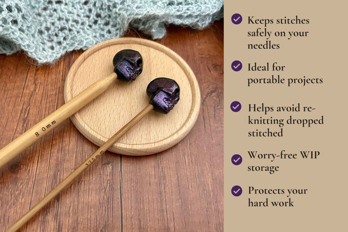 Two wooden knitting needles with dark purple skull-shaped tips resting on a round wooden coaster, set on a wooden table next to a knitted lace cloth. A beige text panel on the right lists product benefits. Ideal for portable projects. Helps avoid re-knitting dropped stitches. Fits mm to 2.5mm to 8mm needles 
