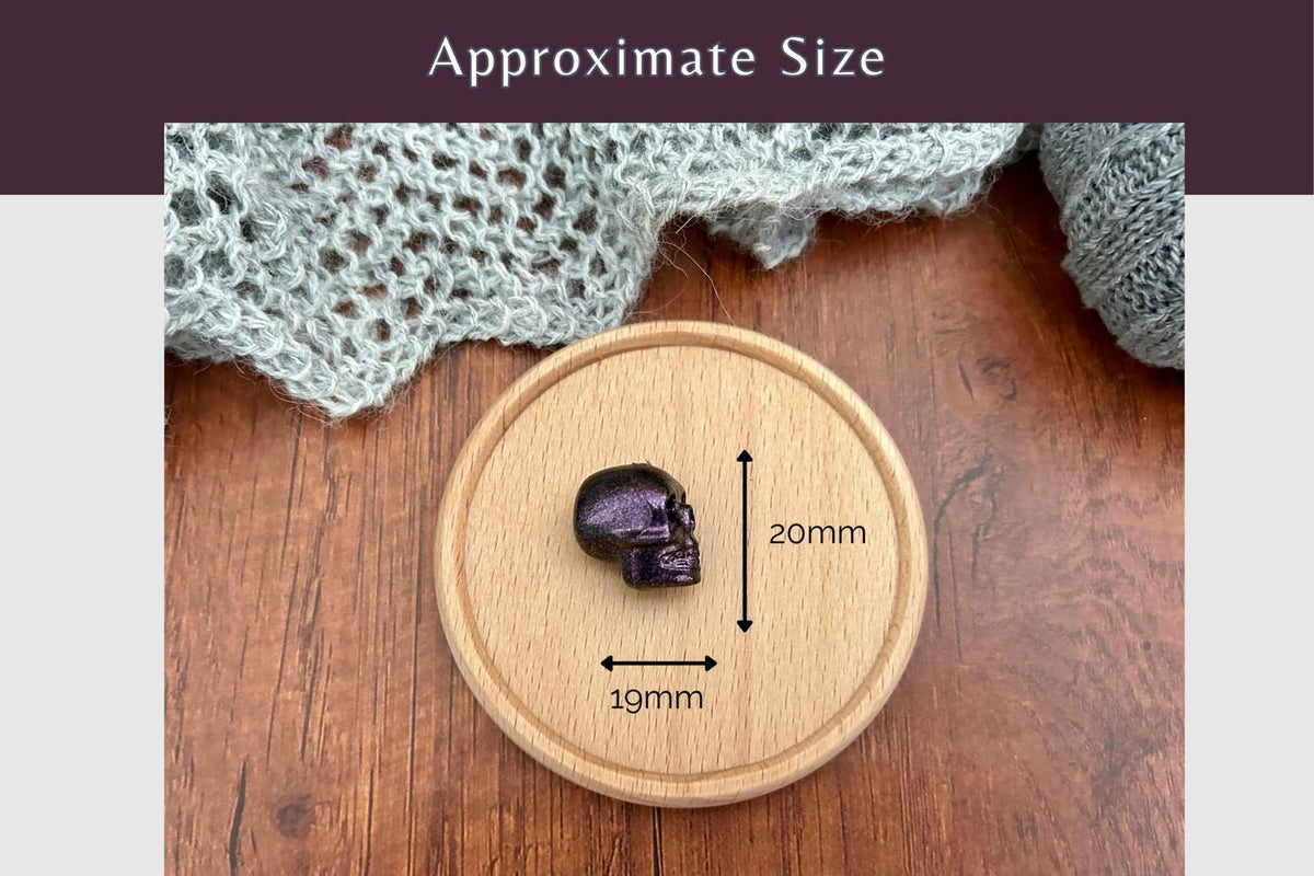 A  skull-shaped stitch saver displayed on a round wooden tray over a wood tabletop, with overlaid arrows and text showing approximate dimensions of 20mm height and 19mm width. A banner at the top reads 'Approximate Size'.