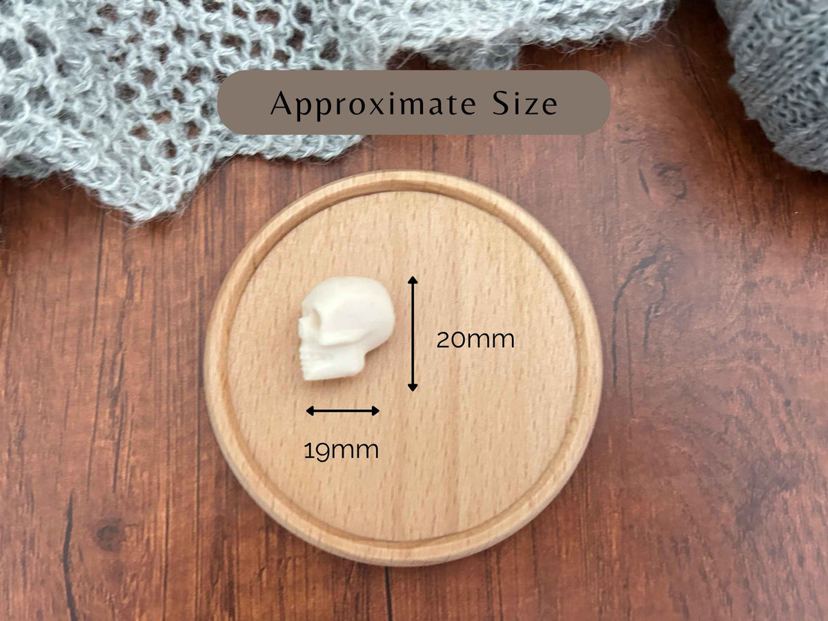 A small off-white skull-shaped stitch saver placed on a round wooden tray over a wood surface, with overlaid arrows and text showing approximate dimensions of 20mm height and 19mm width.
