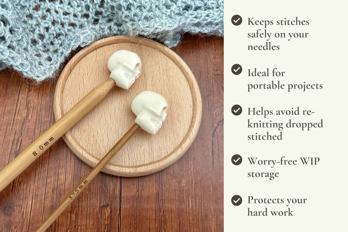 Two wooden knitting needles with skull-shaped tips displayed on a round wooden coaster, with a knitted blue fabric in the background and a text panel listing benefits on the right. Keeps stitches on needles. Ideal for portable projects. Helps avoid re-knitting dropped stitches. Fits mm to 2.5mm to 8mm needles.