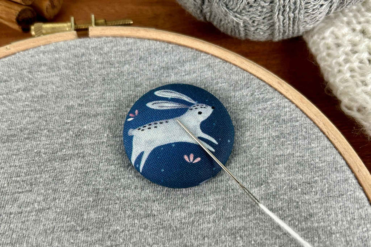 a magnetic needle minder featuring a white rabbit or hare on a dark blue background. A metal needle rests on it