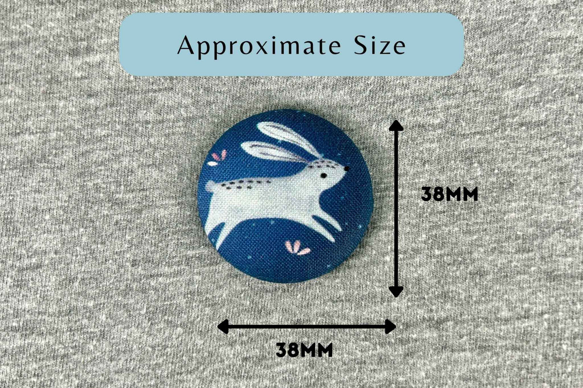 A circular fabric patch with a white rabbit/hare design on a dark blue background, shown on a gray textured surface with measurement arrows and text indicating approximate size 38mm by 38mm.