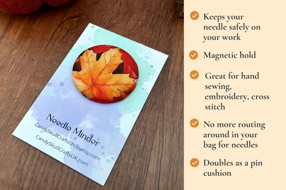A close-up of a magnetic needle minder  featuring a printed autumn maple leaf pattern in red, orange, and yellow, on a backing card with features:  keeps your needle safely on your work. Magnetic hold great for hand sewing, embroidery, cross stitch. No more routing around in your bag looking for needles. Doubles as a pin cushion.
