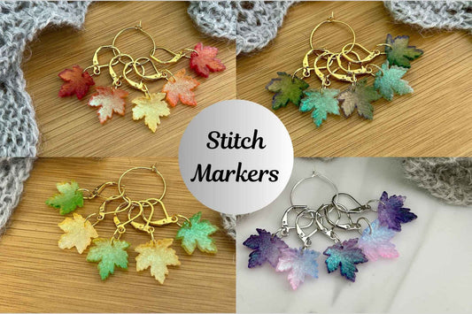 Four sets of maple leaf knitting and crochet stitch markers in 4 colourways to match the seasons, arranged on a wooden surface with a gray crocheted cloth. A central white circle reads 'Stitch Markers'.