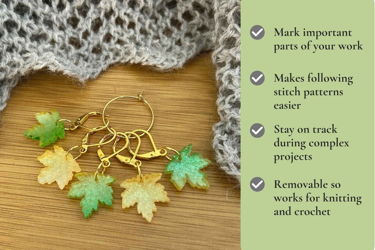 Five green and yellow maple leaf stitch markers, arranged on a wooden surface next to a knitted gray fabric. A light green text panel on the right lists benefits of using stitch markers. Mark important parts of your work, removable so works for knitting and crochet, stay on track on complex projects, makes counting stitches easier.
