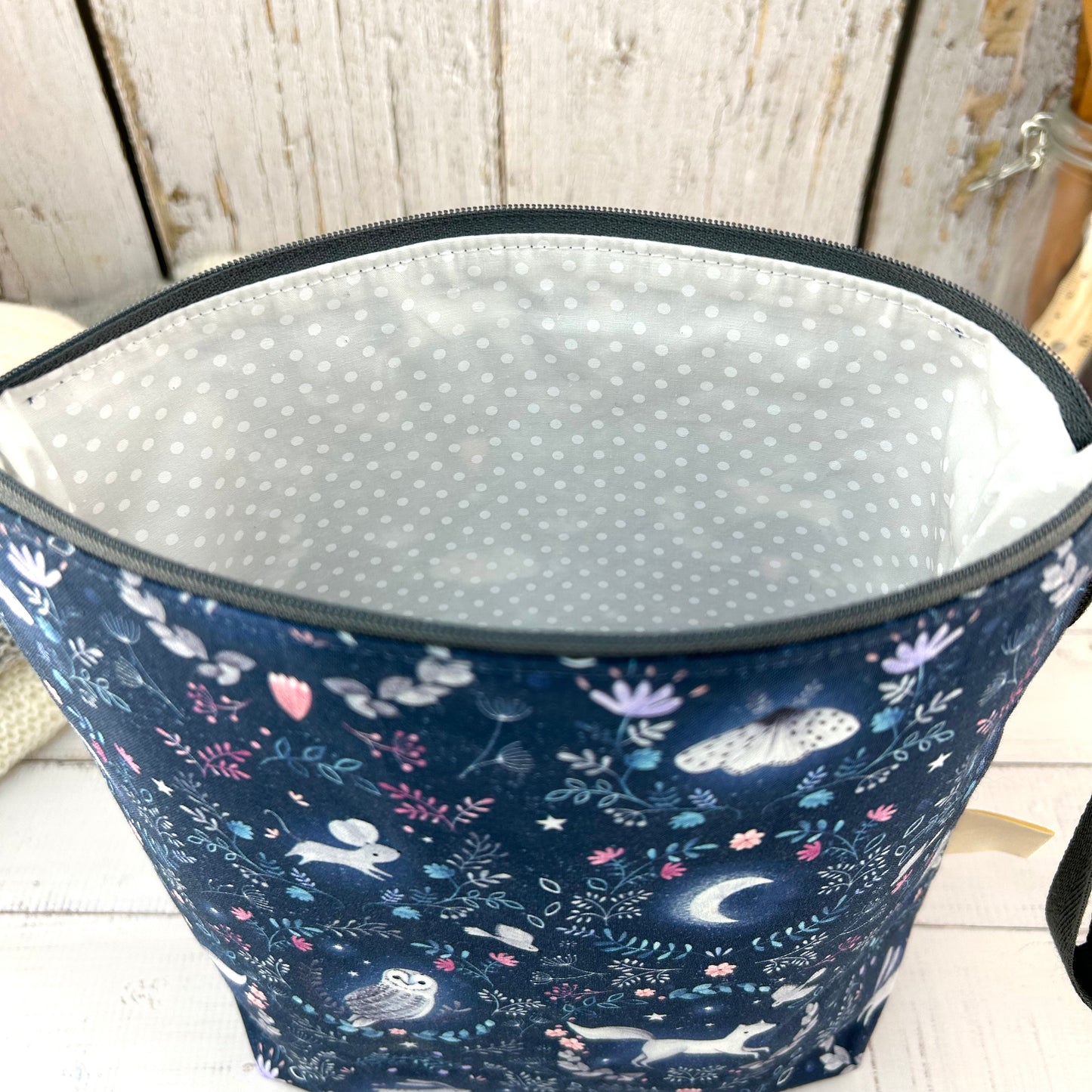 A dark blue knitting or crochet project bag with grey handle & zip. The fabric features nocturnal woodland animals - a hare, fox, moth, and owl. The lining is white with a subtle white spot