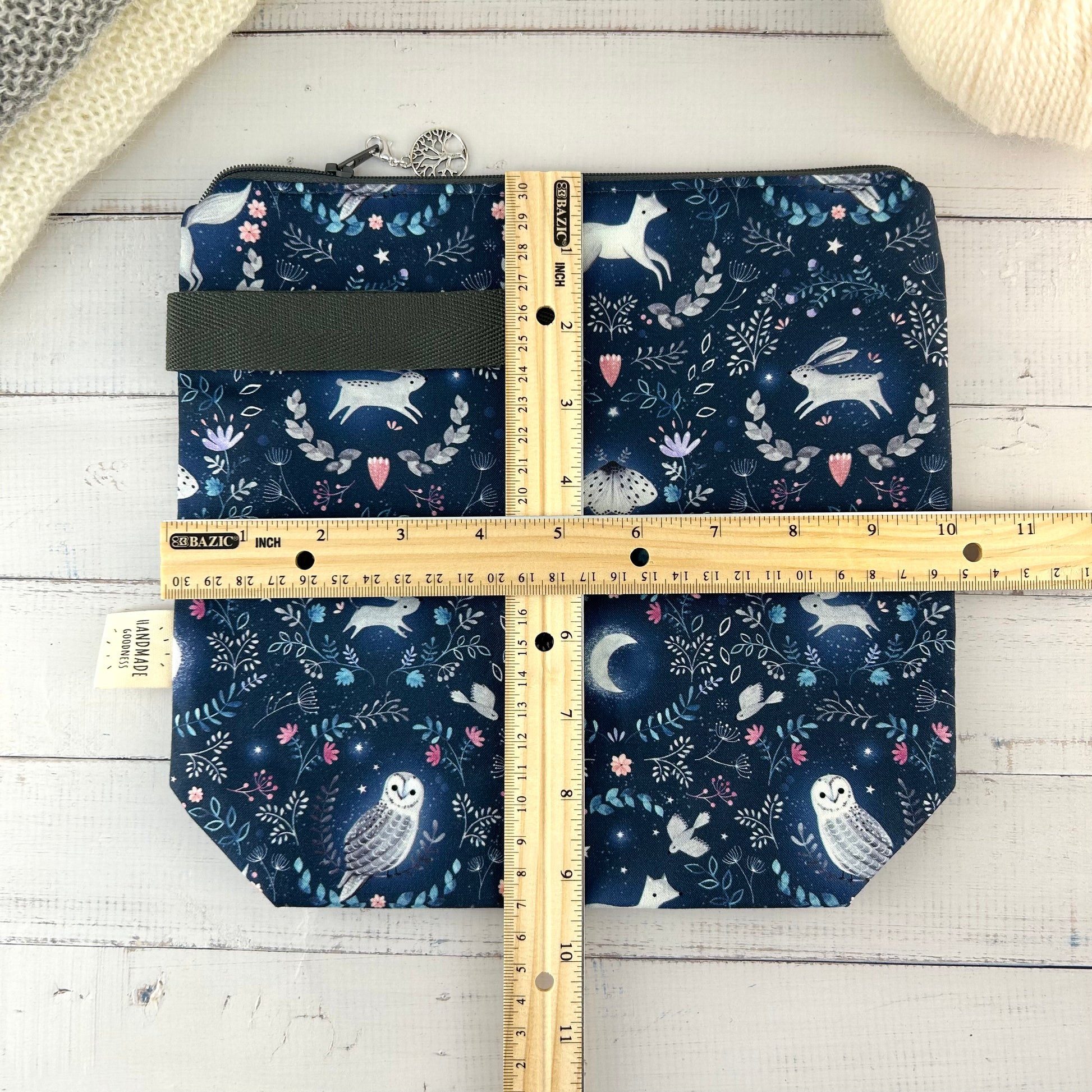 A dark blue knitting or crochet project bag with grey handle & zip. The fabric features nocturnal woodland animals - a hare, fox, moth, and owl. There is a ruler laying across the bag showing it measures approximately 10 inches by 9.5 inches