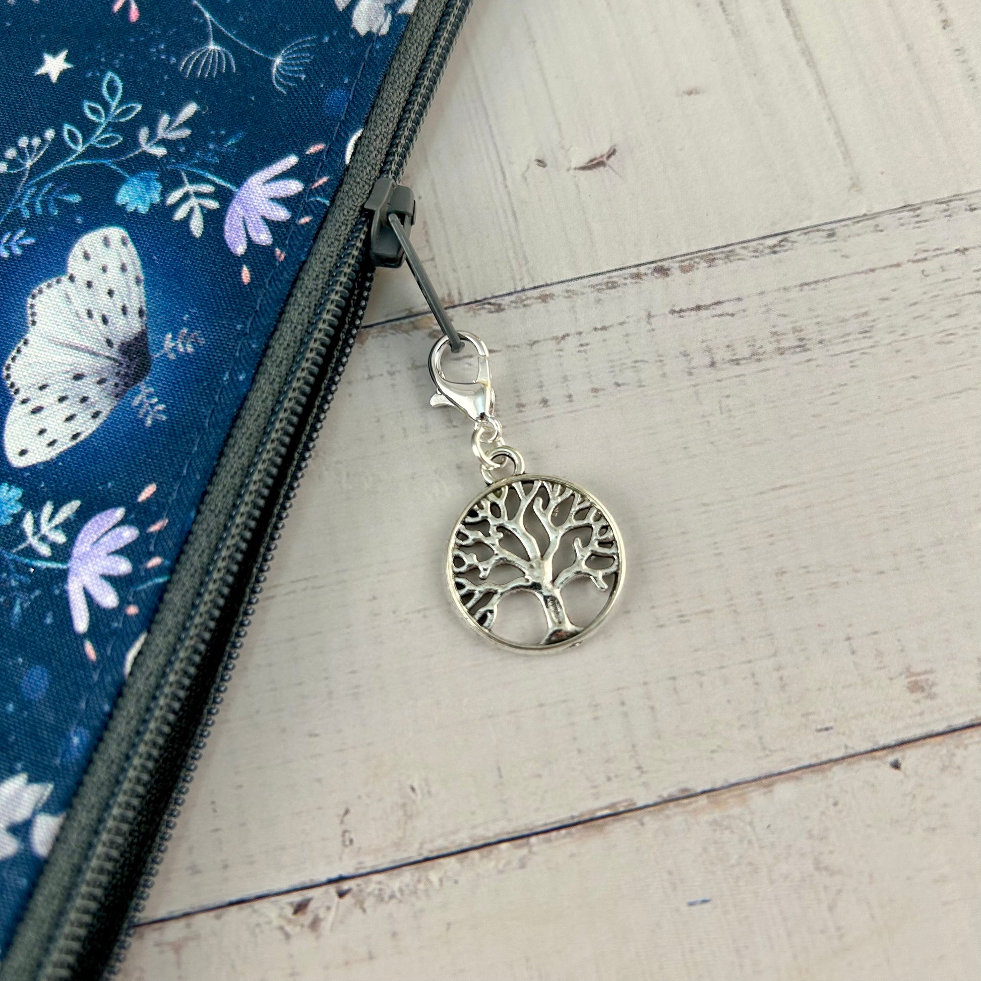 A close up of the zip pull showing a metal tree of life stitch marker/progress keeper attached to the pull