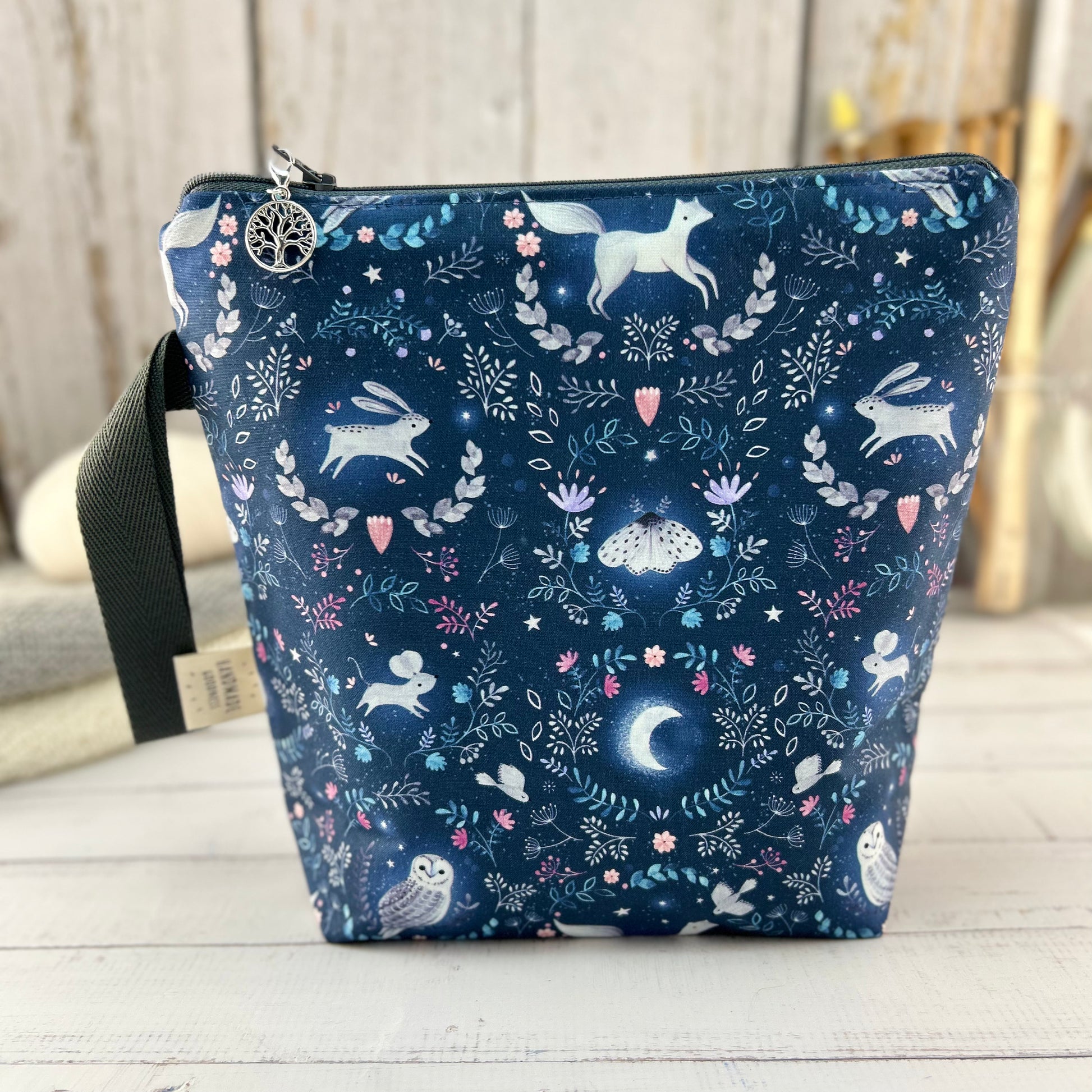 A dark blue knitting or crochet project bag with grey handle & zip. The fabric features nocturnal woodland animals - a hare, fox, moth, and owl