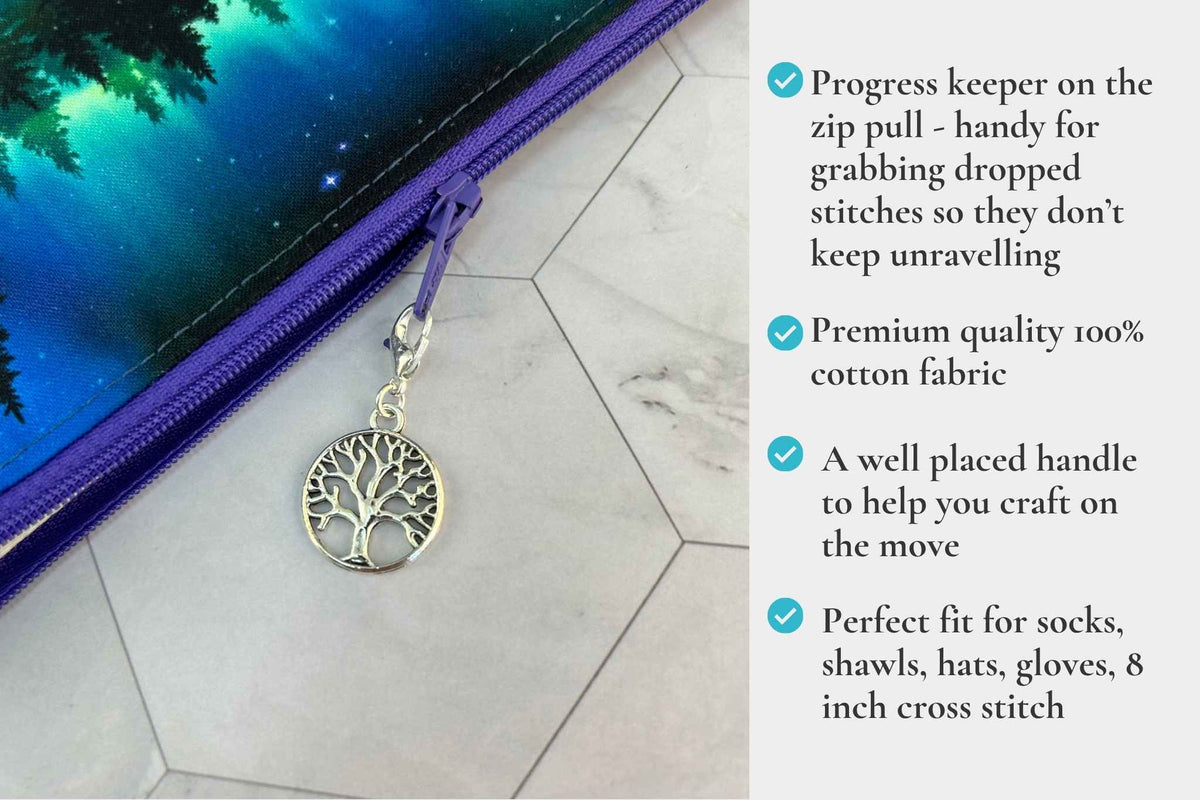 A purple zippered knitting or crochet project bag with a tree-of-life charm zipper pull, shown on a light marble surface next to a printed design, with a text overlay describing the product features. It reads "Progress keeper on the zip pull - handy for grabbing dropped stitches, premium 100% cotton fabric, well placed handle helping you craft on the go, perfect for socks, shawls, hats & gloves"