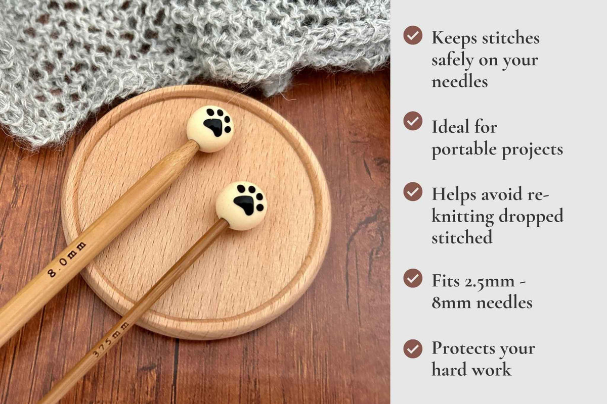 Knitting needles with paw-shaped wooden tips resting on a round wooden tray, with a gray knitted fabric in the background and a text panel on the right listing benefits. Keeps stitches on needles. Ideal for portable projects. Helps avoid re-knitting dropped stitches. Fits mm to 2.5mm to 8mm needles 

