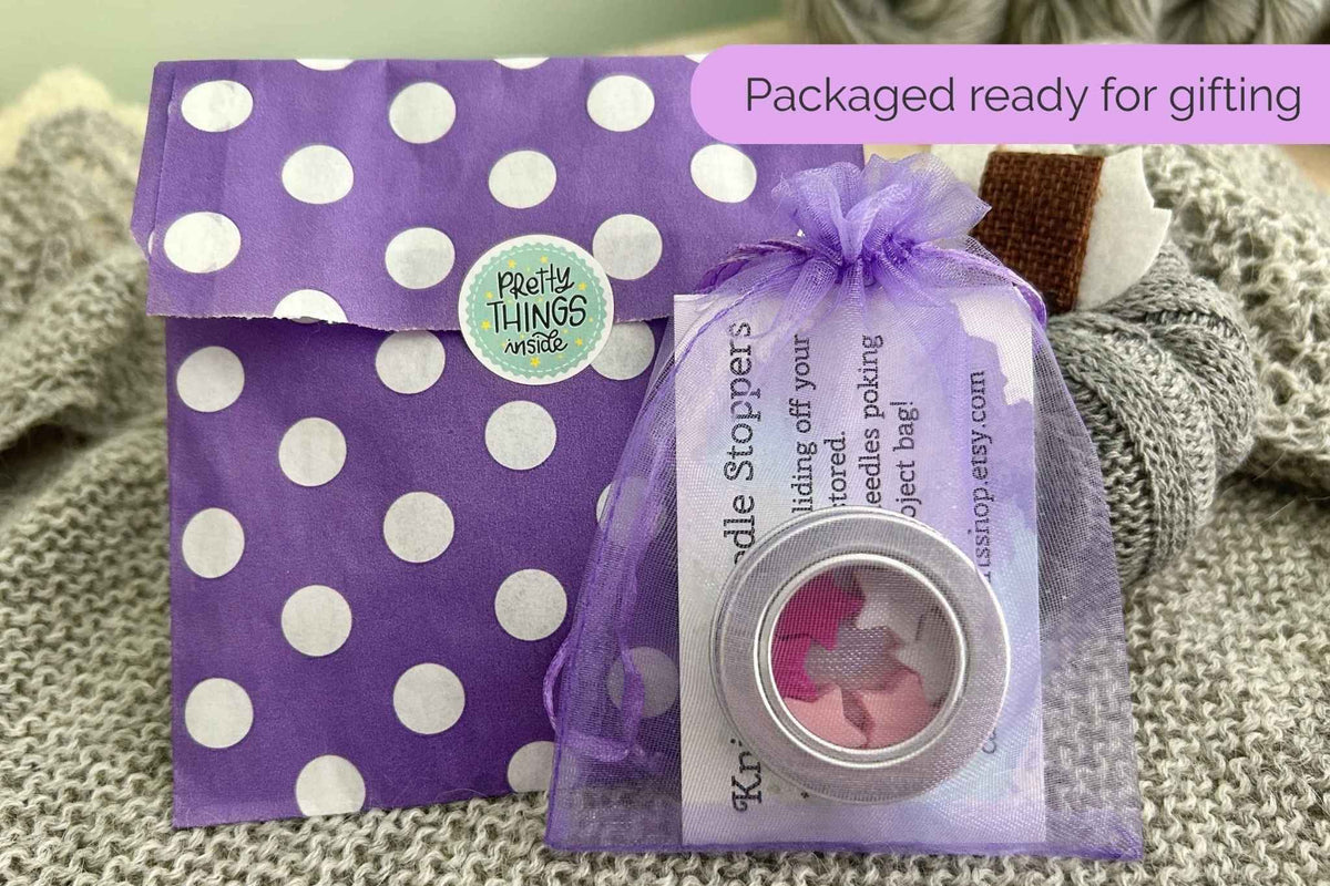 A packaged set of pink star knitting stitch savers, includes a purple polka dot envelope, a lavender organza gift bag with a round metal and an instruction card.