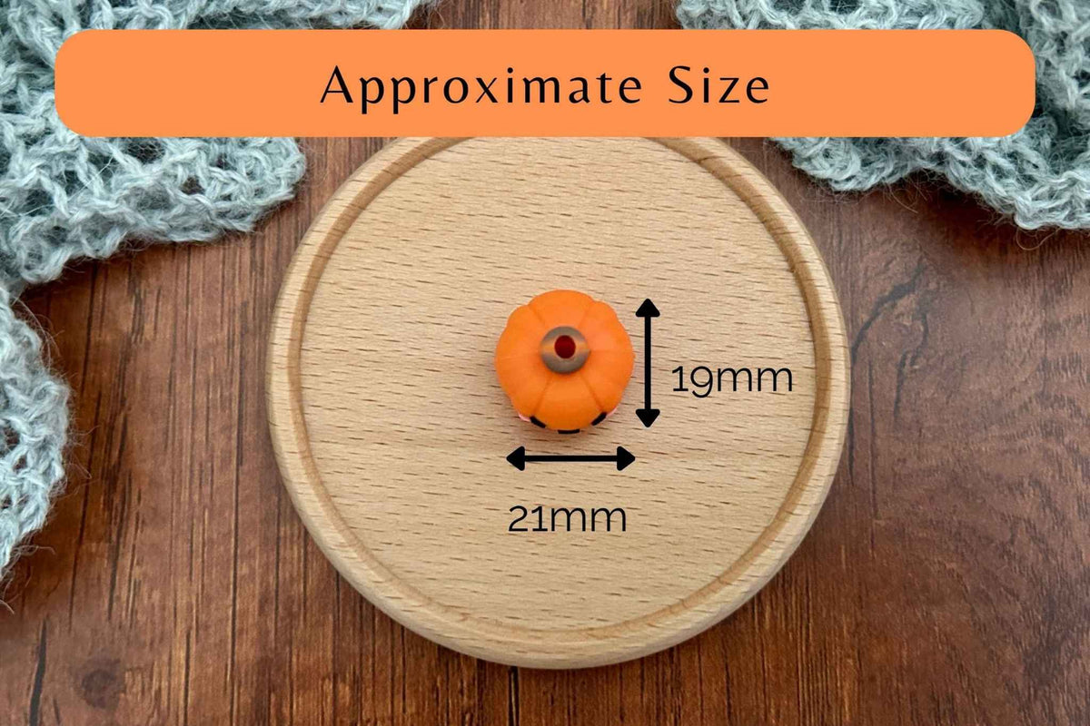 A small orange pumpkin-shaped knitting needle stitch stoppers shown on a round wooden board with overlaid size measurements reading 19mm height and 21mm width, plus an orange label at the top that says 'Approximate Size'.