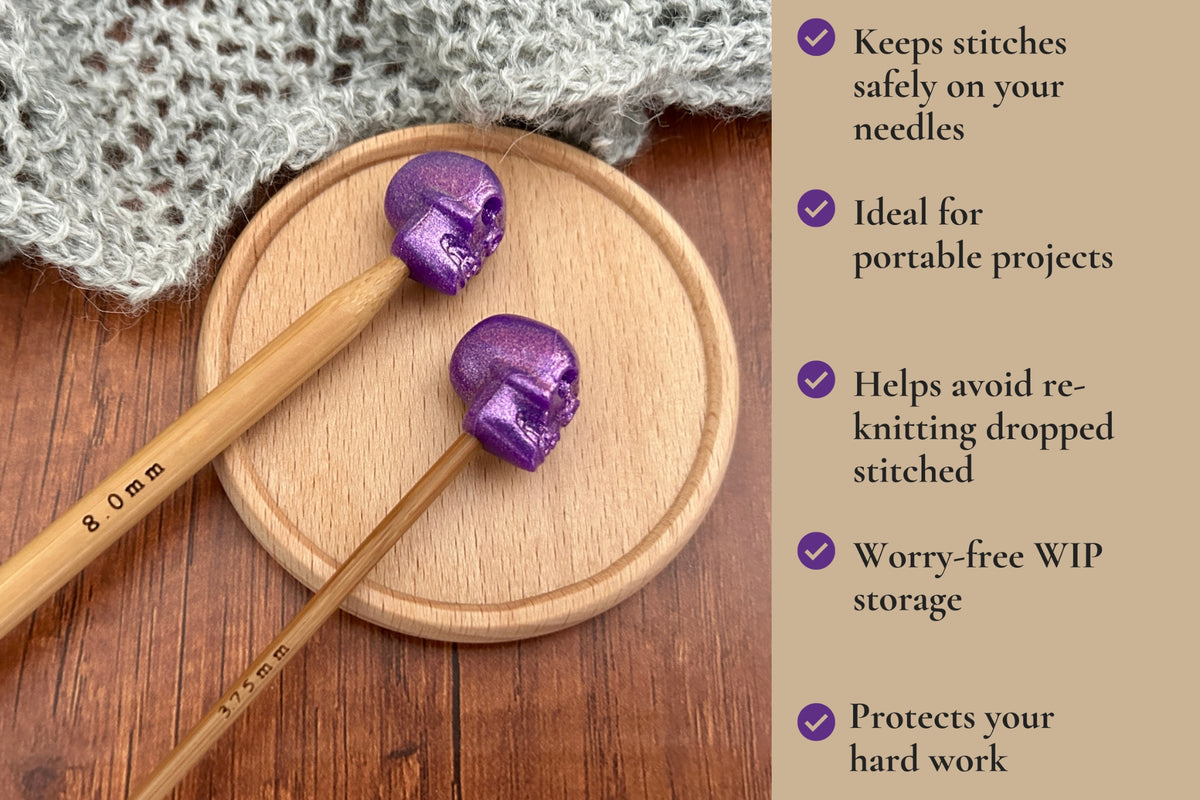 Two wooden knitting needles with purple skull-shaped stitch stoppers or point protectors resting on a round wooden coaster, with a knitted gray fabric and a text panel listing benefits on the right. Keeps stitches safely on needles, ideal for portable projects, helps avoid dropped stitches