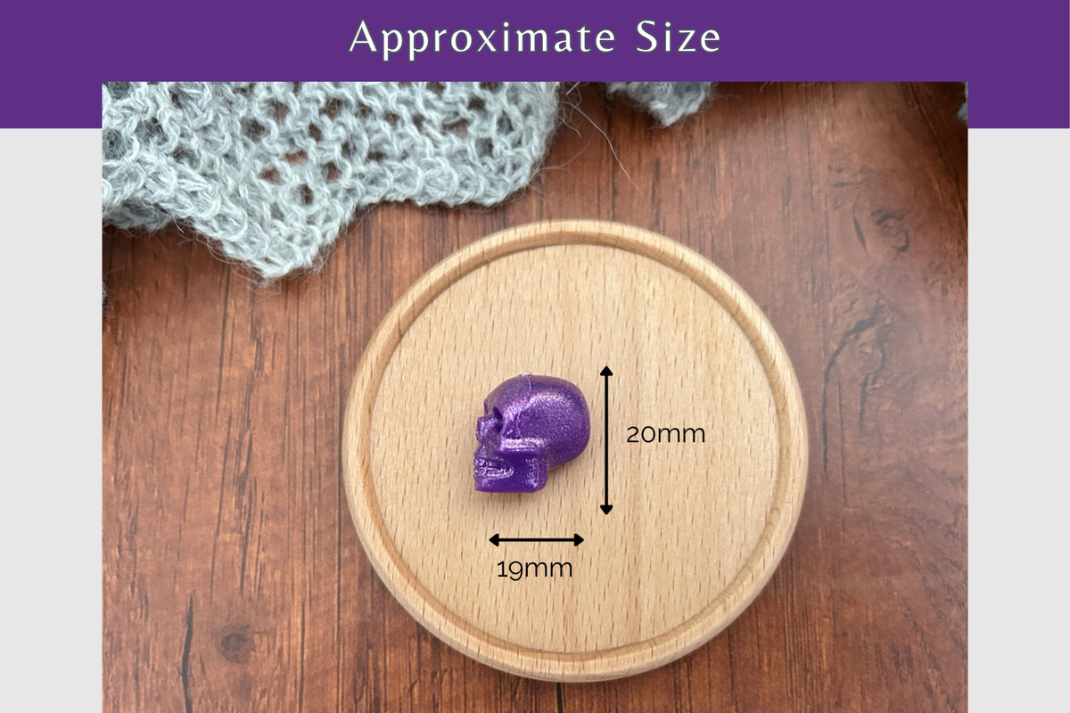 A small shimmery purple skull-shaped needle stopper placed on a round wooden tray, with overlaid dimension arrows and text reading 20mm height and 19mm width, plus a purple header that says 'Approximate Size'.