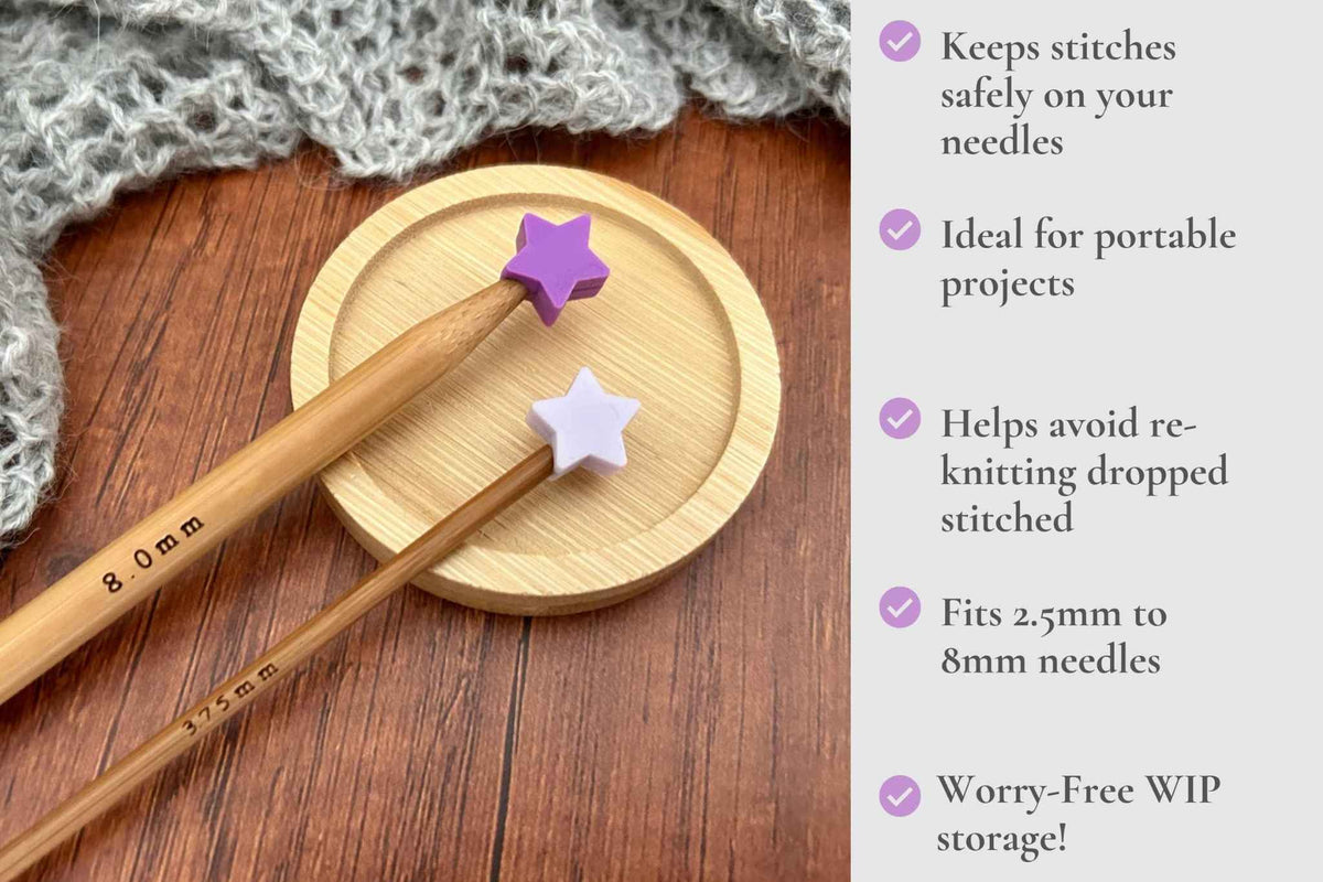 Two wooden knitting needles with purple and white star-shaped stitch holders resting on a round wooden coaster, set on a wooden table next to a gray knitted scarf. A text panel on the right lists product features with purple check marks which read: Keeps stitches on needles. Ideal for portable projects. Helps avoid re-knitting dropped stitches. Fits mm to 2.5mm to 8mm needles 

