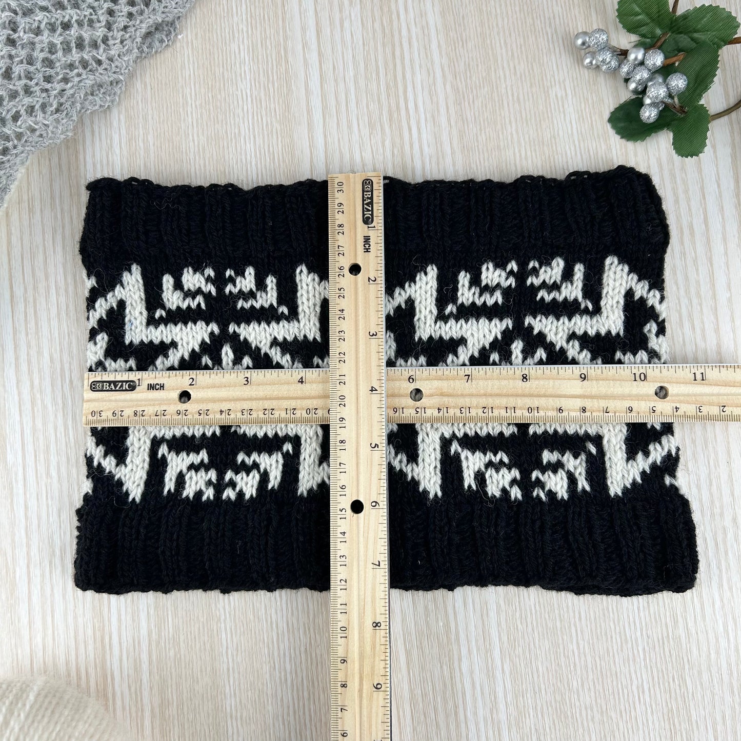 A black knit cowl or neck warmer with a traditional Norwegian stranded colourwork design of the Selbu Rose / Star, styled on a wooden table with measurements show as 10.5 inches by 7.5 inches