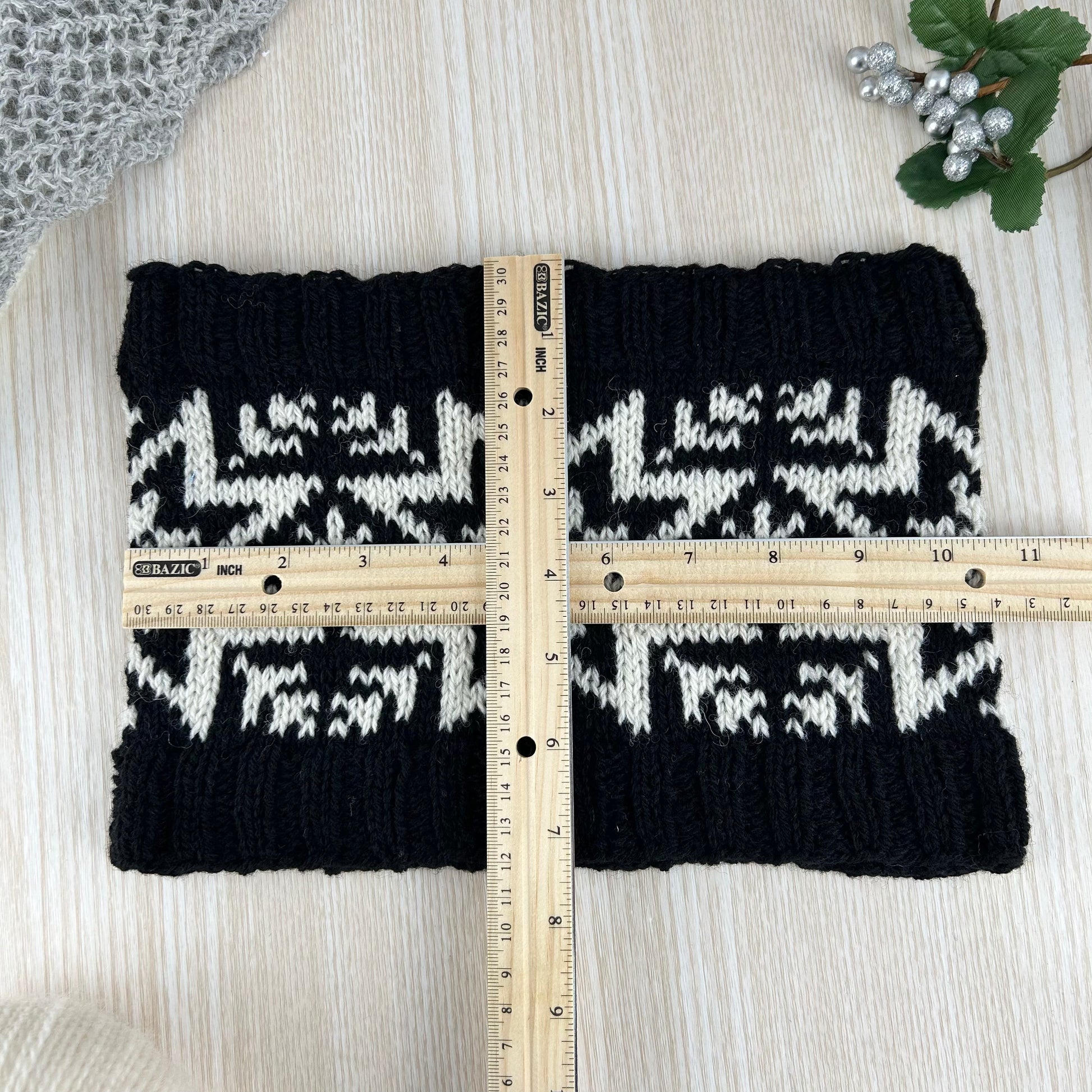 A black knit cowl or neck warmer with a traditional Norwegian stranded colourwork design of the Selbu Rose / Star, styled on a wooden table with measurements show as 10.5 inches by 7.5 inches