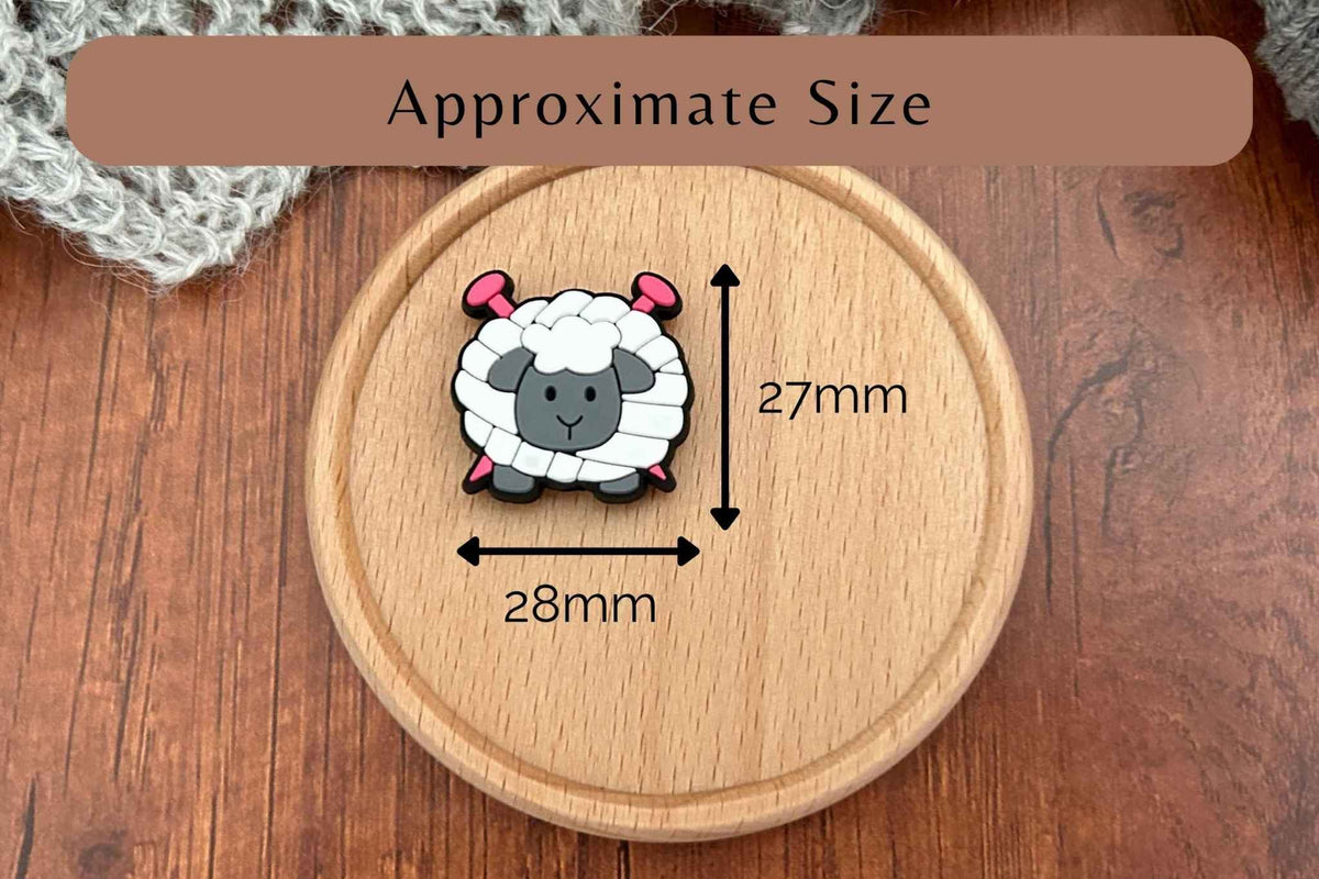 A small cartoon sheep-shaped knitting needle stopper shown on a round wooden board with measurement arrows and labels reading 27mm and 28mm, plus a banner that says Approximate Size.