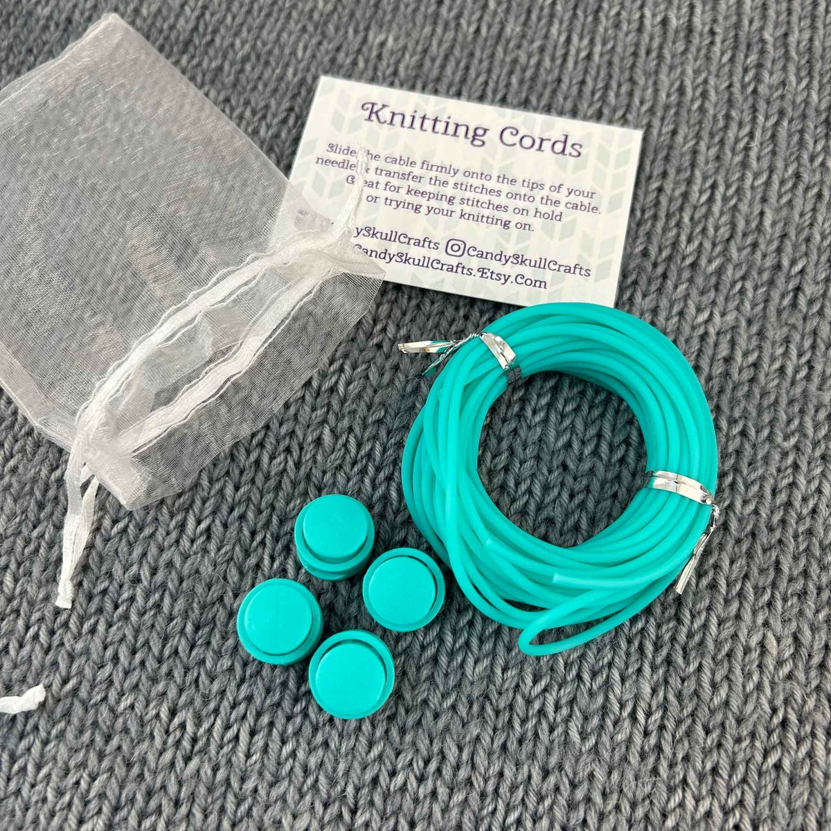 A set of sea green coiled knitting stitch holder cords and 4 stoppers. The instruction card and organza mesh bag are shown in the background